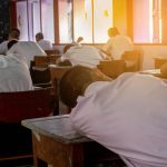 Poor Student with studentâ€™s uniform so tired of the exam. Lying down on the arm in the classroom. Sleepy student  fall asleep during  test at noon in the hot season.